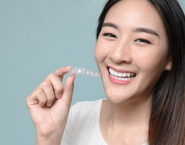 Woman smiling and holding SureSmile clear aligner