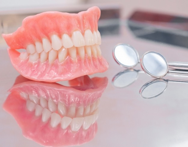 Full dentures on reflective surface next to dental mirror