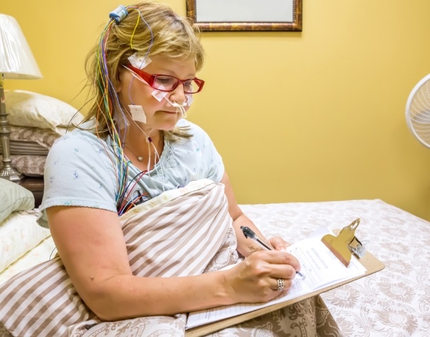 Woman writing on clipboard while hooked up to device for sleep test