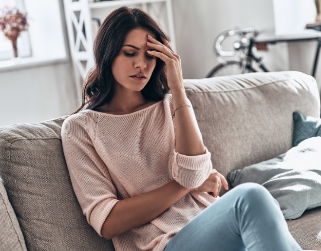 Tired woman sitting on couch and touching forehead